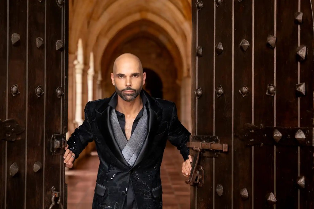 Hombre vestido elegante saliendo de unas puertas grandes en una arquitectura antigua.