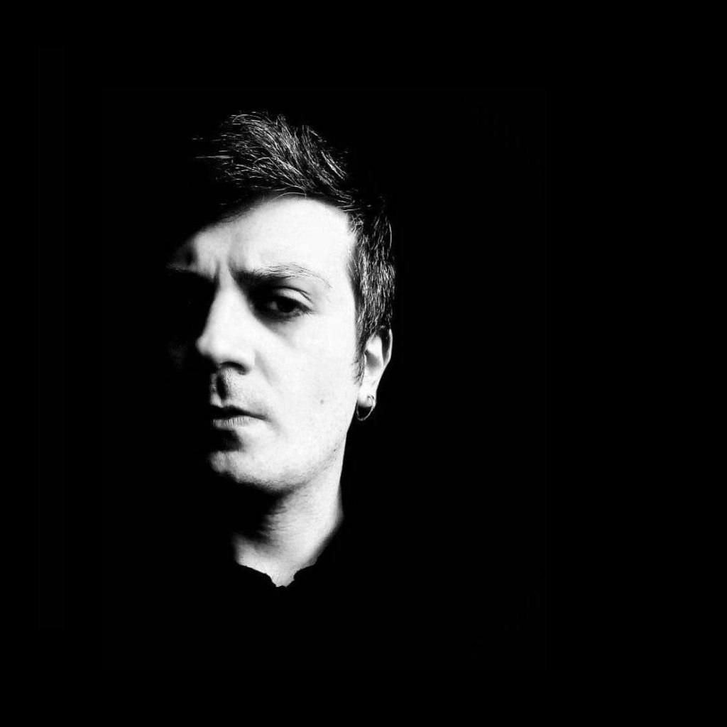 Retrato en blanco y negro de un hombre con expresión seria, iluminado parcialmente sobre un fondo negro.